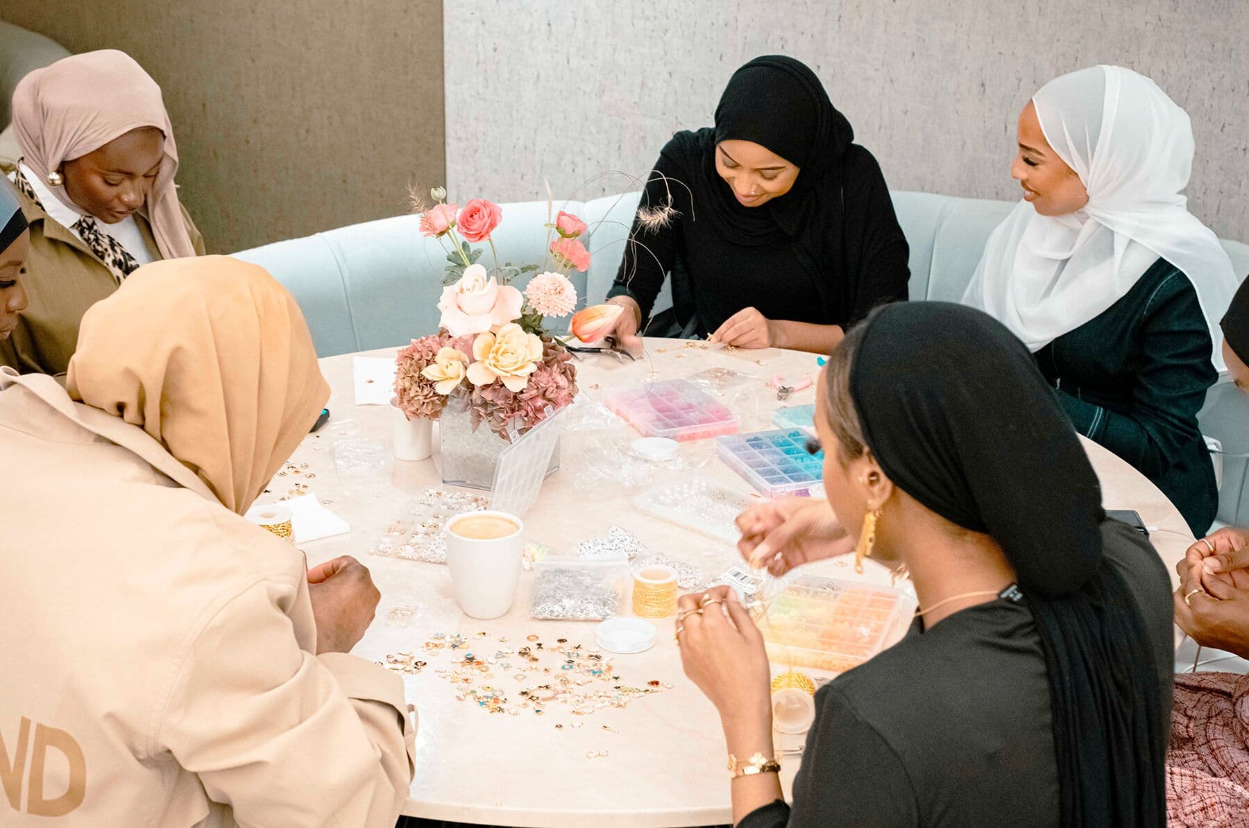 Friends gathered around a table with flowers, making bracelets together