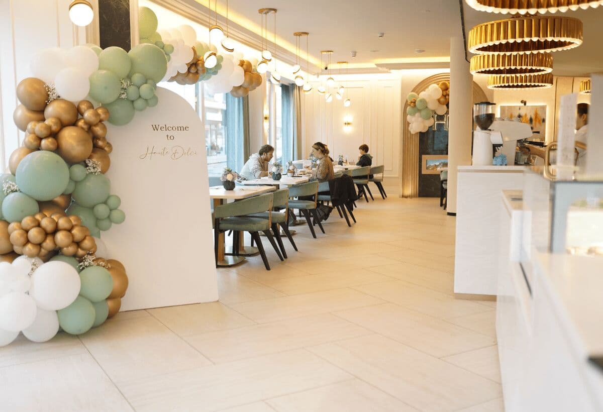 A Haute Dolci dining room dressed for an event, with a sage, white and gold balloon arch and a welcome sign