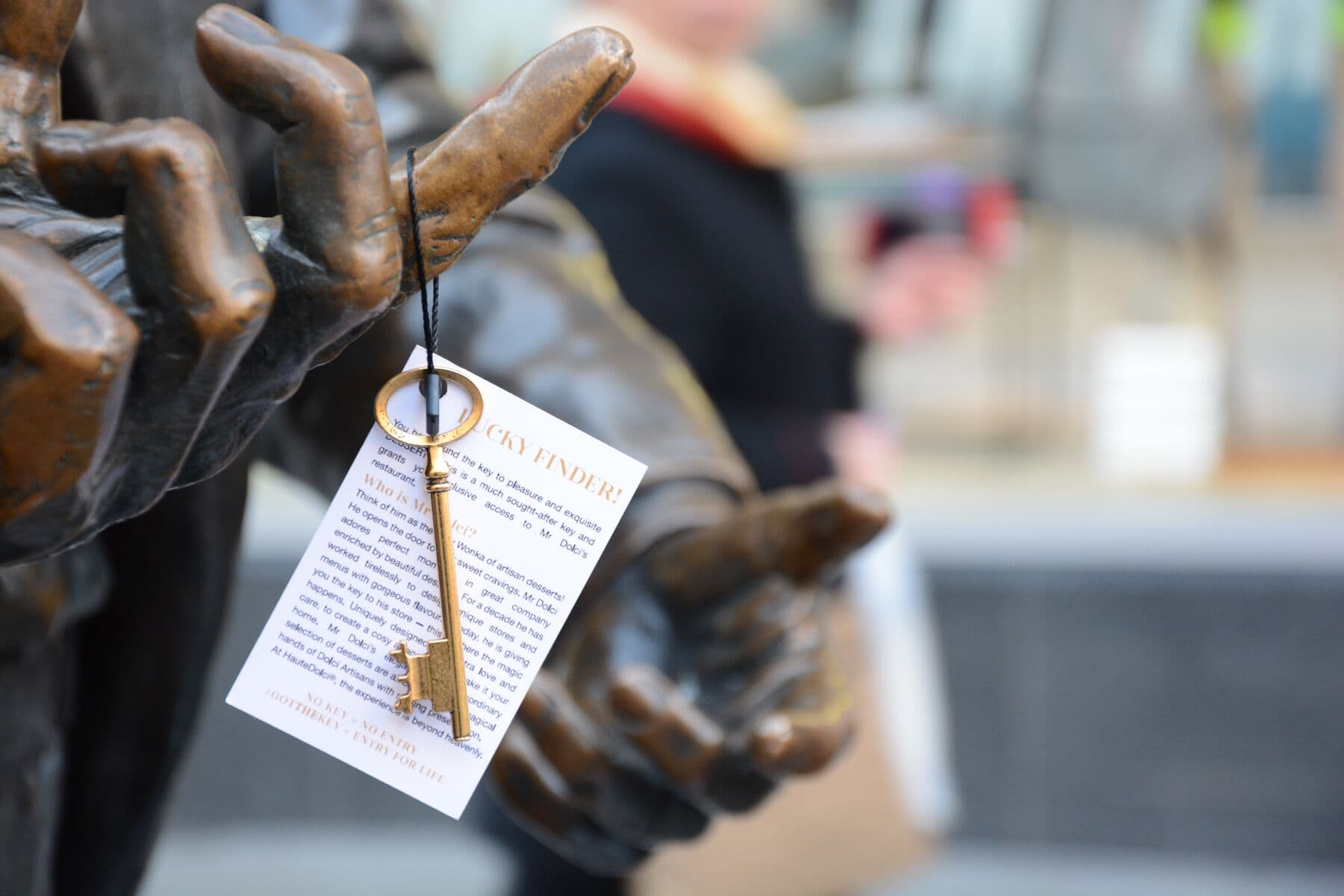 A golden HD Key on its tag, hanging from the hand of a bronze statue