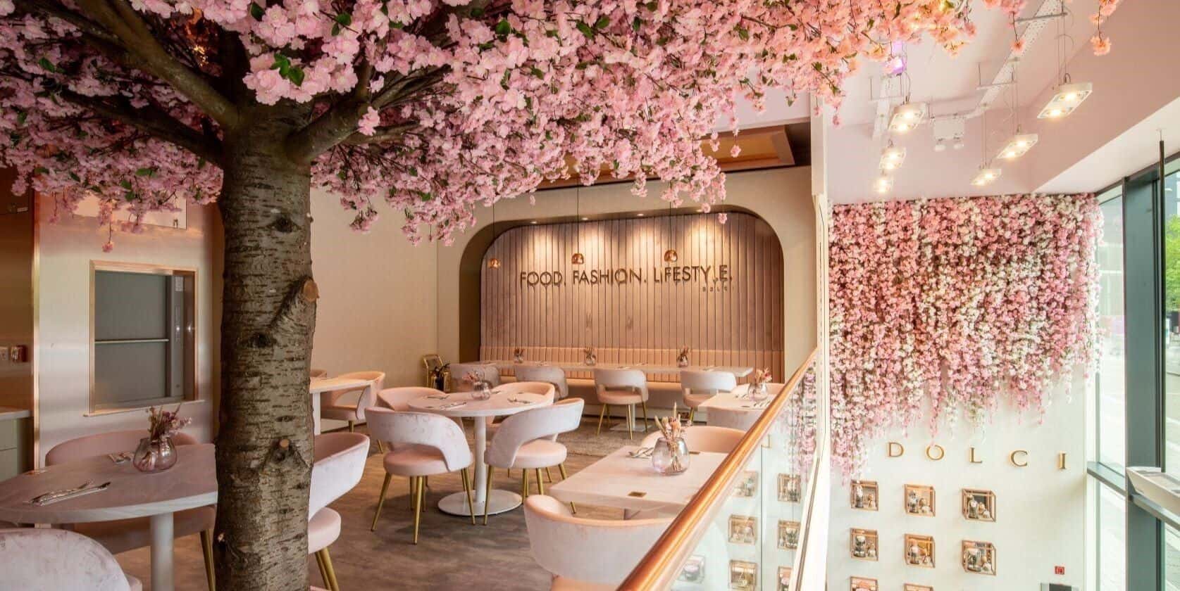 Inside Haute Dolci Wembley: pink cherry-blossom trees arching over blush chairs and marble tables